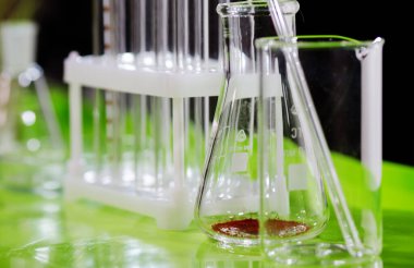 Test tüpleri, mataralar ve diğer cihazlar laboratuvardaki masanın üzerinde duruyor..