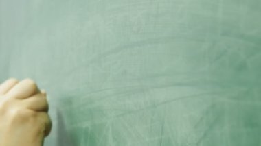 Okutman tahtaya tebeşirle yazıyor. Okutman elin yakın plan çekimi..