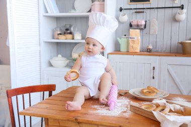 Baby cooking homemade cakes. Early spring, Easter and a little girl in the chef's costume in the kitchen bakes bread and biscuits. The girl got dirty with flour. Mom's helper clipart