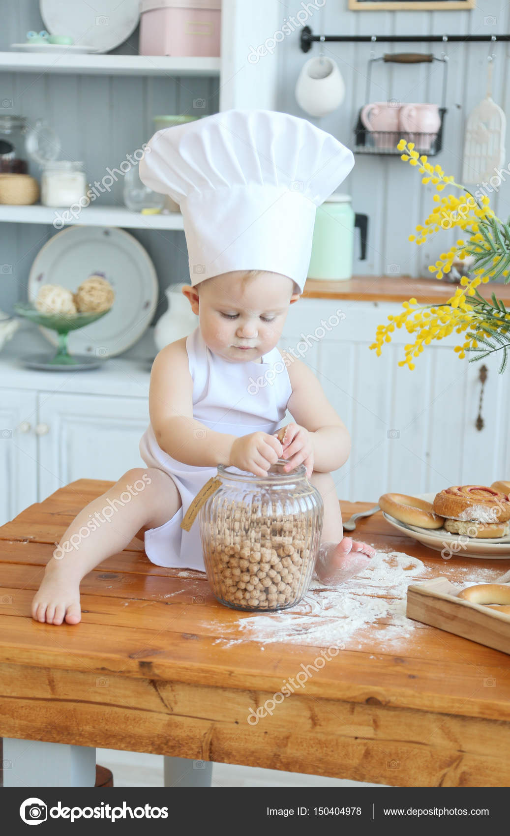 Baby cooking homemade cakes. Early spring, Easter and a little girl in the  chef's costume in the kitchen bakes bread and biscuits. The girl got dirty  with flour. Mom's helper Stock Photo
