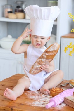 Baby cooking homemade cakes. Early spring, Easter and a little girl in the chef's costume in the kitchen bakes bread and biscuits. The girl got dirty with flour. Mom's helper clipart