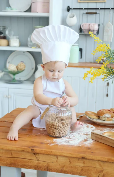 Baby cooking homemade cakes. Early spring, Easter and a little girl in the chef's costume in the kitchen bakes bread and biscuits. The girl got dirty with flour. Mom's helper — Stock Photo, Image