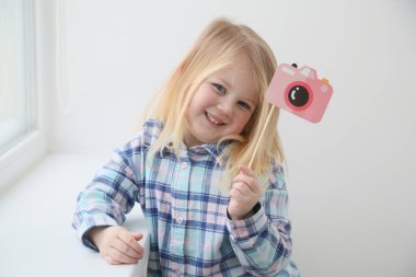 The child with a toy photo camera, which is a picture. This girl is a cute blonde kid/ She is smiling. This is an illustration for photo class for preschooler or English school. Isolate, copy space.