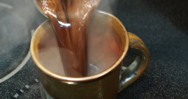 Turkish coffee preparation. Brewed hot coffee is poured from cezve into cup