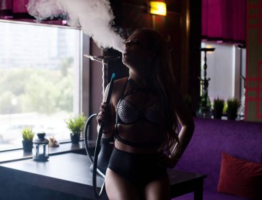 Seksi sarışın deri esaret içinde nargile sigara içiyor.