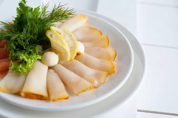 Fish sliced in a white dish with lemon, butter, dill and parsley. Placed on a white wooden plank table — Stock Photo, Image