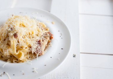 Bir beyaz tahta masada beyaz bir tabak makarna carbonara