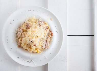 Bir beyaz tahta masada beyaz bir tabak makarna carbonara