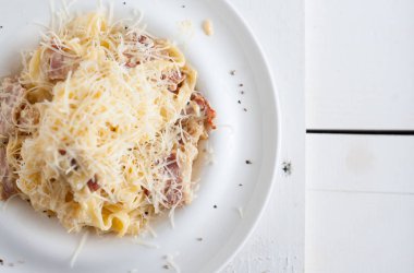 Bir beyaz tahta masada beyaz bir tabak makarna carbonara