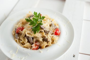 Beyaz bir tabak içinde mermer sığır eti ile makarna. Beyaz ahşap tahta masanın üzerine yerleştirilen