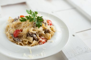 Beyaz bir tabak içinde mermer sığır eti ile makarna. Beyaz ahşap tahta masanın üzerine yerleştirilen