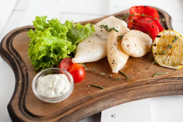 Grilled squid with lemon, sauce and vegetables and herbs. Placed on a wooden dark board — Stock Photo, Image