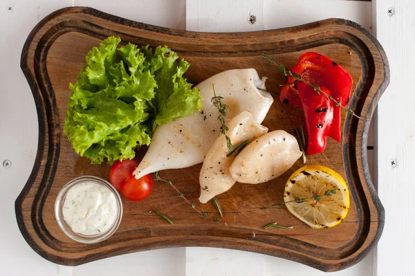 Grilled squid with lemon, sauce and vegetables and herbs. Placed on a wooden dark board — Stock Photo, Image