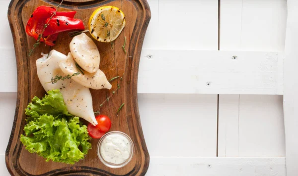 Grilled squid with lemon, sauce and vegetables and herbs. Placed on a wooden dark board — Stock Photo, Image