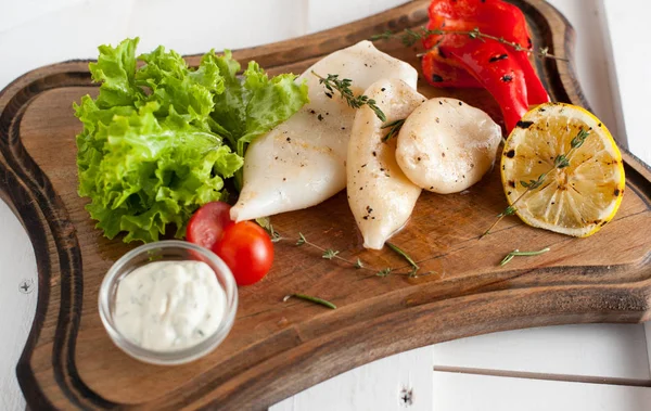 Grilled squid with lemon, sauce and vegetables and herbs. Placed on a wooden dark board — Stock Photo, Image