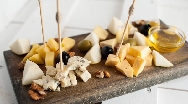 Assorted variety of cheese with honey and nuts. Placed on a dark wooden board — Stock Photo, Image