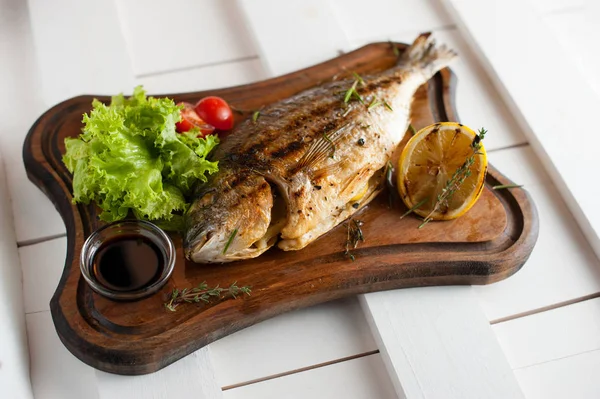 Grilled fish Dorado on a wooden board with lemon, salad, sauce and cherry tomatoes — Stock Photo, Image