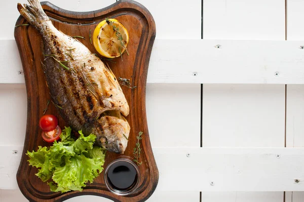Grilled fish Dorado on a wooden board with lemon, salad, sauce and cherry tomatoes — Stock Photo, Image