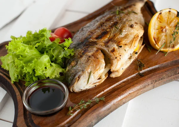 Grilled fish Dorado on a wooden board with lemon, salad, sauce and cherry tomatoes — Stock Photo, Image