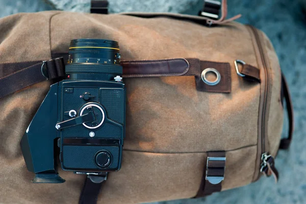 La cámara de formato medio de la película se encuentra en las piedras contra el telón de fondo de una mochila vintage de lona —  Fotos de Stock