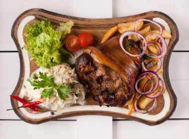 Lahana, patates, soğan ve yeşillik bir ahşap kesme tahtası üzerinde pişmiş domuz knuckle. Yukarıdan görüntülemek