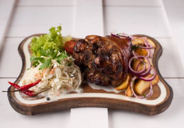 Lahana, patates, soğan ve yeşillik bir ahşap kesme tahtası üzerinde pişmiş domuz knuckle