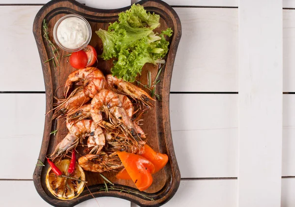 Fried tiger shrimps with lemon, vegetables, sauce and greens on a wooden cutting board. View from above — Stock Photo, Image