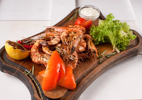 Fried tiger shrimps with lemon, vegetables, sauce and greens on a wooden cutting board — Stock Photo, Image