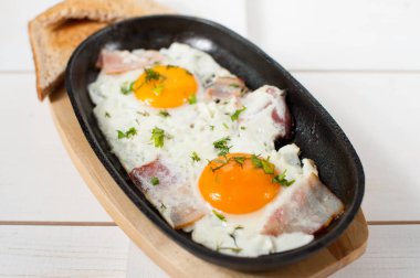 Omlet pastırma ve taze otlar ile bir tencerede kızartılır. Ekmek tost ile hizmet