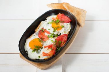 Sahanda yumurta taze domates ve taze otlar ile bir tencerede kızartılır. Ekmek tost ile hizmet