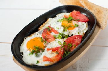 Sahanda yumurta taze domates ve taze otlar ile bir tencerede kızartılır. Ekmek tost ile hizmet