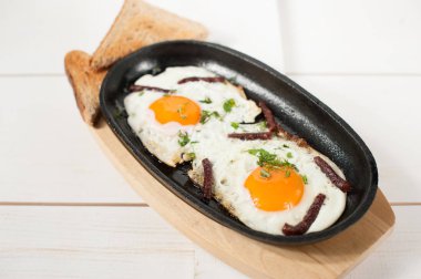 Omlet tütsülenmiş sosis ve taze otlar ile bir tencerede kızartılır. Ekmek tost ile hizmet