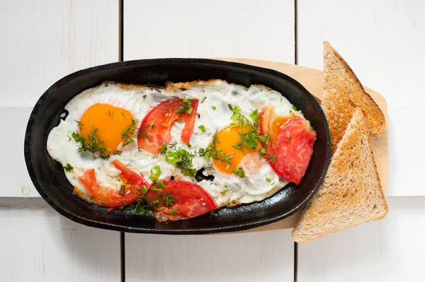 Scrambled eggs with fresh tomatoes and fresh herbs fried in a pan. Served with bread toast — Stock Photo, Image