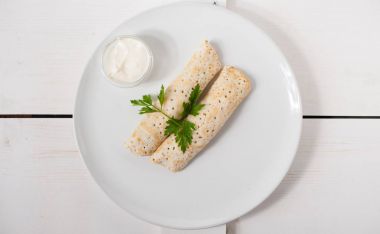 Ekşi krema ve beyaz bir plaka üzerinde taze maydanoz ile geleneksel doldurulmuş krep