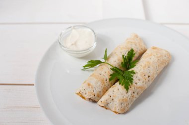 Ekşi krema ve beyaz bir plaka üzerinde taze maydanoz ile geleneksel doldurulmuş krep