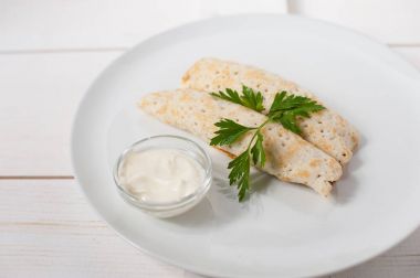 Ekşi krema ve beyaz bir plaka üzerinde taze maydanoz ile geleneksel doldurulmuş krep