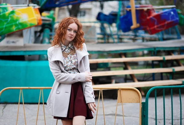 Sexy fille aux cheveux roux avec des taches de rousseur dans un collier vintage se dresse sur le fond d'un vieux parc d'attractions — Photo