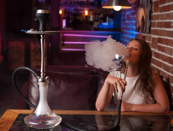 Menina bonita em uma blusa branca fuma um narguilé no interior do bar — Fotografia de Stock