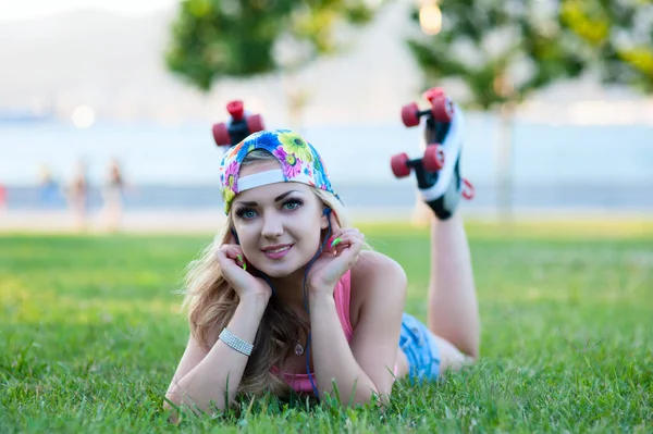 Sexy jovem loira menina em rolos vintage deitado no gramado no parque e ouvir música em fones de ouvido — Fotografia de Stock