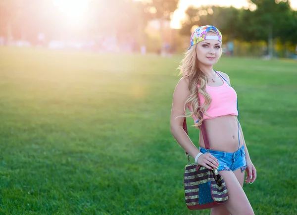 Menina loira jovem sexy em shorts jeans fica em um gramado em um parque de verão — Fotografia de Stock