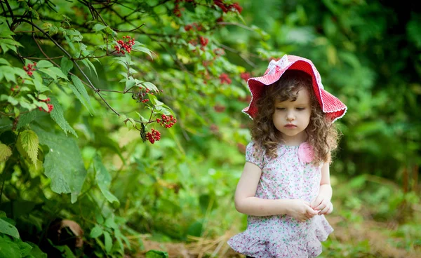 Chica rizada de tres años de edad en sombrero rojo caminando en el parque de verano — Foto de Stock