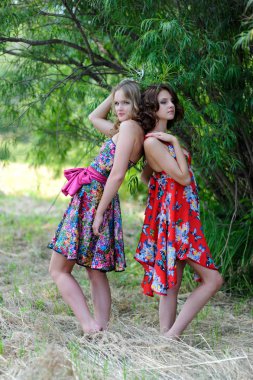 İki genç sarışın kız ve parlak elbiseler ağaçlarının fonunda bir yaz parkta poz kahverengi saçlı bir kadın