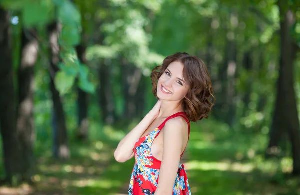 Jeune fille brune en robe rouge posant sur l'allée dans le parc d'été contre les arbres — Photo