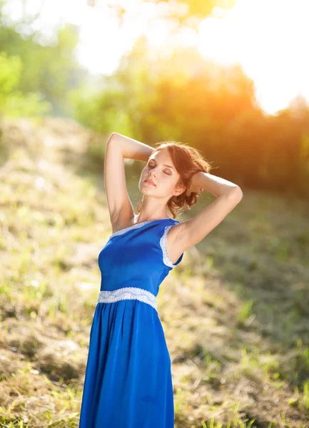 Fiatal lány, barna hajú nő egy kék ruhás pózol egy parkban fényes nap sugarai — Stock Fotó