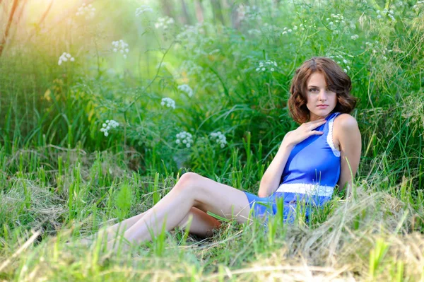 Junges brünettes Mädchen in blauem Kleid posiert auf Gras liegend im Sommerpark — Stockfoto