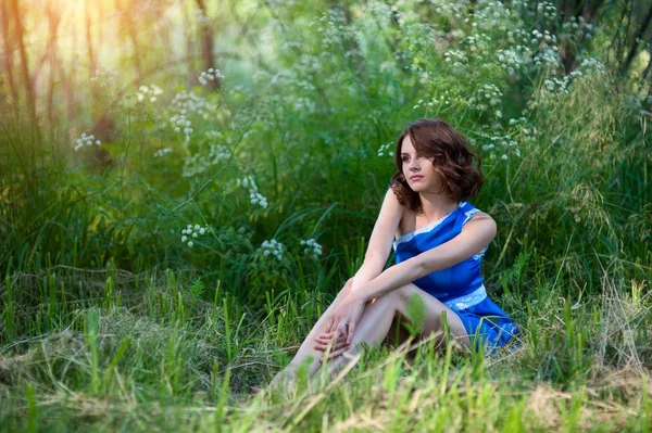 Junges brünettes Mädchen in blauem Kleid posiert auf Gras liegend im Sommerpark — Stockfoto