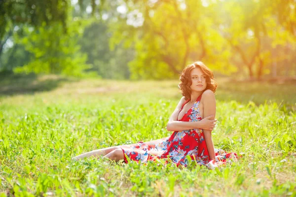 年轻的黑发女孩穿着红色的裙子在夏日公园的草地上摆着太阳 — 图库照片