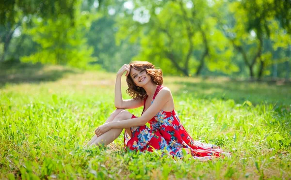 年轻的黑发女孩穿着红色的裙子在夏日公园的草地上摆着太阳 — 图库照片