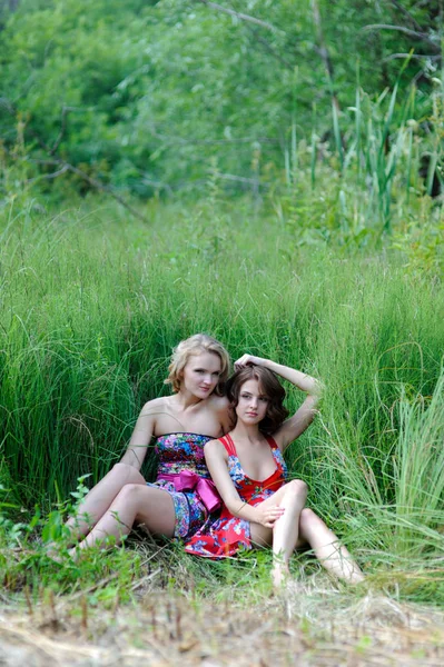 Deux jeunes filles blondes et femme aux cheveux bruns dans des robes lumineuses posant dans un parc d'été dans de l'herbe haute — Photo