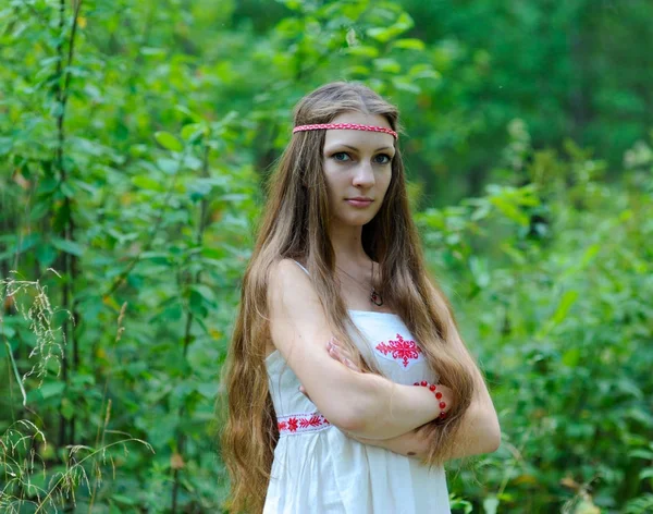 Portrait of a young beautiful Slavic girl with long hair and a Slavic ethnic dress on a background of green grass — Stock Photo, Image